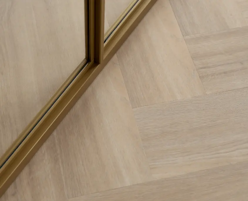 Detail van een lichte PVC visgraatvloer bij een gouden deurprofiel